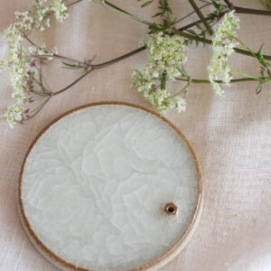 round, flat object on a white cloth background. The object has a flat but textured surface and is off-shite in colour. 