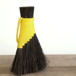 Dark brown arenga fibre brush with bright yellow hemp cord binding. Shown on a rustic wooden table against a white backdrop.