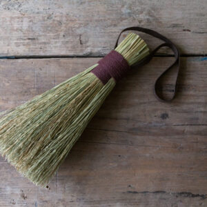 natural fibre hand brush bound with a brown cotton  handle. Shown on a light, weathered table. 