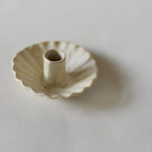 small, off-white circular candleholder with a scalloped edge. Shown against a white background. 