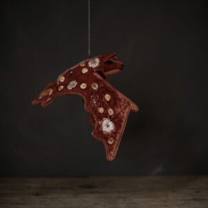 A dark rustic orange coloured fabric bat which has been embroidered with brightly coloured flowers. Shown hanging above a wooden table against a very dark background. 
