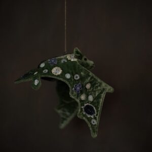 A green silk velvet textile bat, heavily embroidered with flower details. Shown against a very dark background.
