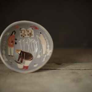 A small blue ceramic bowl, hand illustrated with two people in an idyllic rural setting