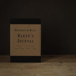 a black book with a brown paper belly band. Shown on a rustic wooden table top. 