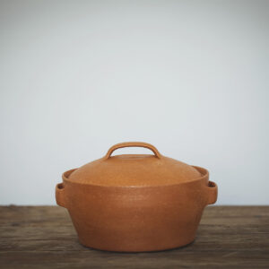 Terracotta cooking pot on a wooden table against a neutral backdrop 