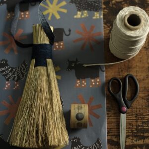 slate grey wrapping paper by Lilly Hedley decorated with lino cut prints of farm animals. Shown with a hand brush by Rosa Harradine, tape, scissors and string. 