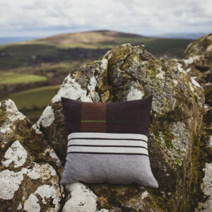 Dark and light blue striped cushion shown against a craggy Welsh hillside 