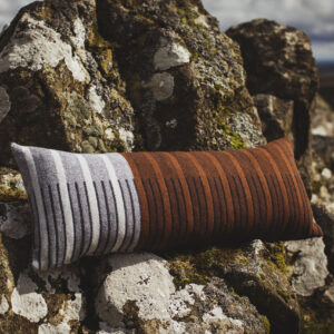 long, bolster style cushion in brown and grey. Photographed against a craggy Welsh hillside. 